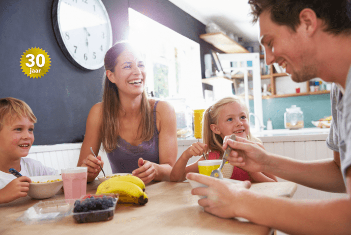 Een gezin met twee kinderen zit glimlachend aan de ontbijttafel